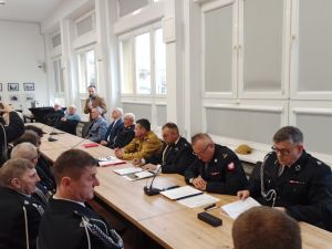 Na zdjęciu znajdują się strażacy siedzący przy stole, przemawia Wiceburmistrz Miasta.
