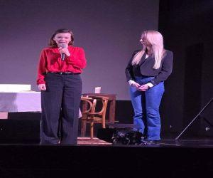 dwie panie na scenie jedna mówiąca przez mikrofon